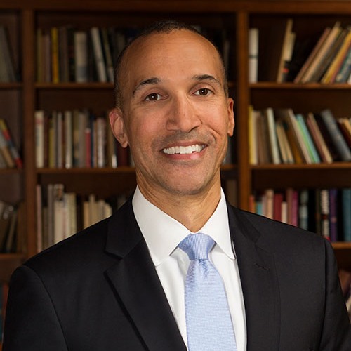 head and shoulders portrait of logan powell adult in business suit standing in front of a bookshelf